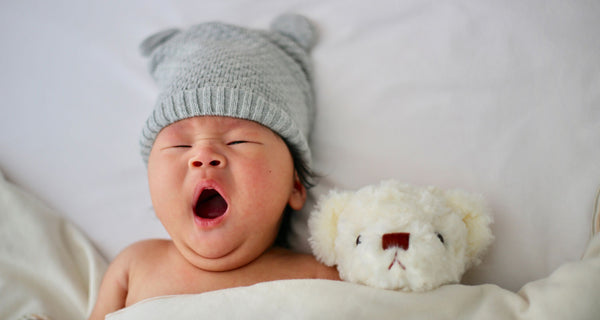 Neonato che sbadiglia e indossa un cappello. Credito Unsplash Minnie Zhou.