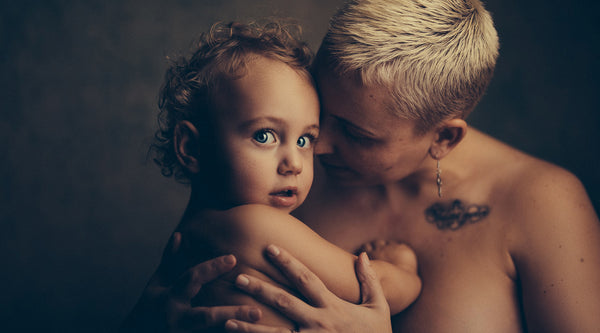 Shirtloze vrouw die haar huid-op-huid baby vasthoudt ©Janko Ferlic voor Unsplash. 